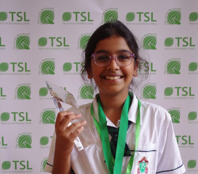 A young student holds a glass trophy and smiles, with a medal around their neck